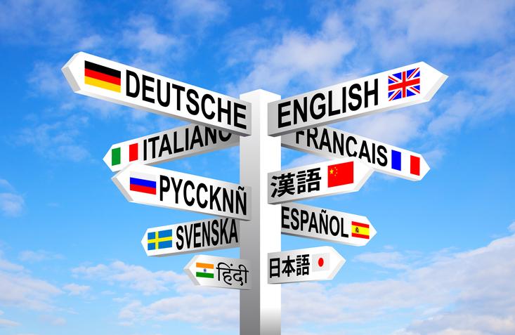 Multilingual languages and flags sign post against blue sky.
